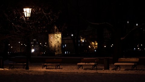 
 street light lantern and snowy sidewalk with cobblestone and park benches and background of world from passing cars in me at night