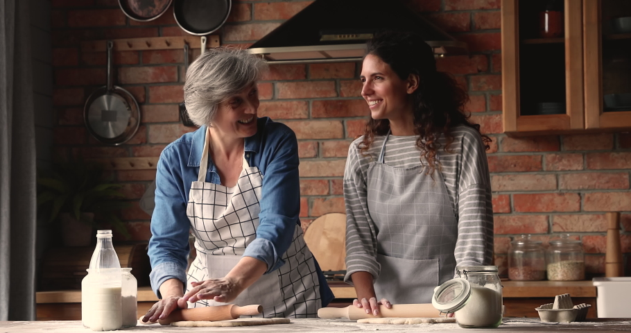 Elderly woman her grown up daughter preparing dough, flattening it with rolling-pin for bakery, talk laughing enjoy cookery and communication in cozy kitchen. Two generation women family hobby concept Royalty-Free Stock Footage #1067355148