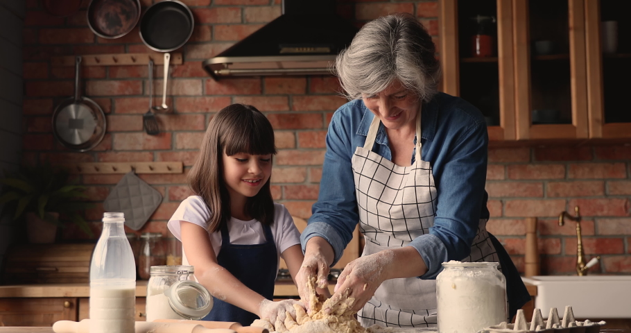 Elderly 60s grandmother preparing with little pretty granddaughter family recipe pie, kneading with hands dough talking enjoy process. Older generation teach younger, hobby and cookery at home concept Royalty-Free Stock Footage #1067355163