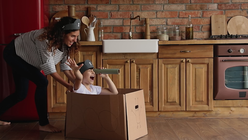 Young mother ride little cute daughter sit in carton box, kid girl looking in paper tube binocular enjoy creative game with mom in kitchen. Creativity, handmade plaything, having fun at home concept Royalty-Free Stock Footage #1067355169