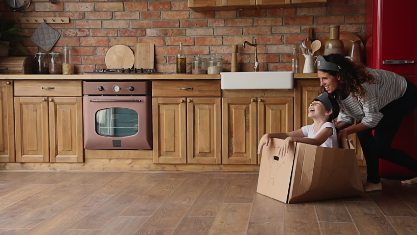 Active family play games at modern warm kitchen, young mom riding small daughter while she sitting inside of cardboard box, celebrate relocation day to new home, spend quarantine time creative concept Royalty-Free Stock Footage #1067355175