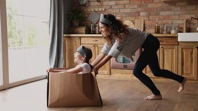Active family play games at modern warm kitchen, young mom riding small daughter while she sitting inside of cardboard box, celebrate relocation day to new home, spend quarantine time creative concept - Powered by Shutterstock - Get 15% off with code: PIKWIZARD15