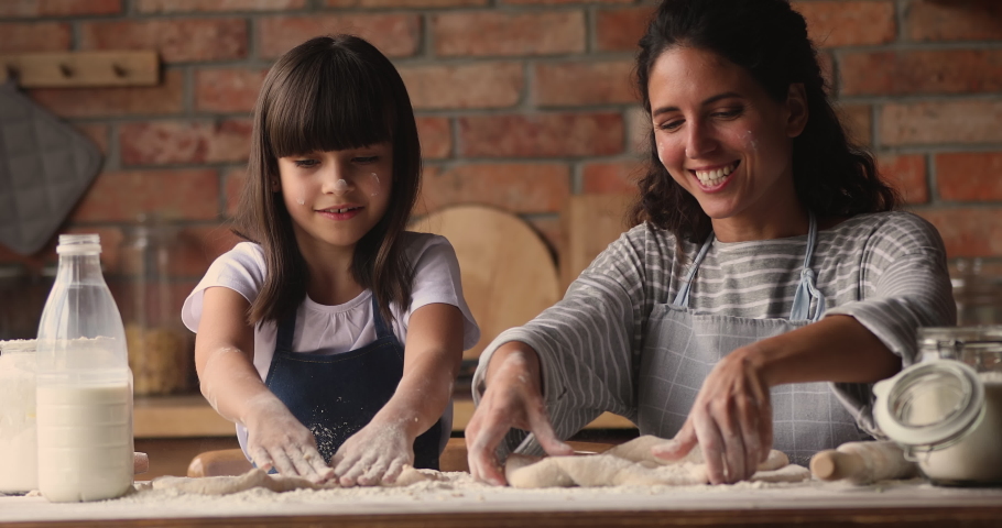 Loving young mom and little cute daughter cooking kneading dough with hands together in cozy kitchen, kid girl enjoy cookery process, smears mom nose with flour having fun while prepare bakery at home Royalty-Free Stock Footage #1067355181