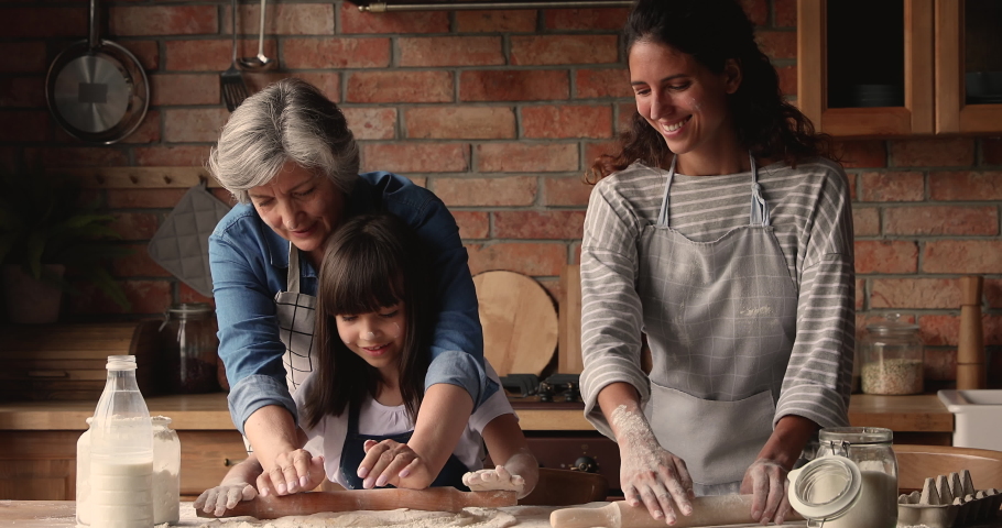 Three gen women in apron cooking together in kitchen, elderly granny, grown up daughter little granddaughter prepare pie, flattening dough enjoy process. Transfer skills from generation to gen concept Royalty-Free Stock Footage #1067355184