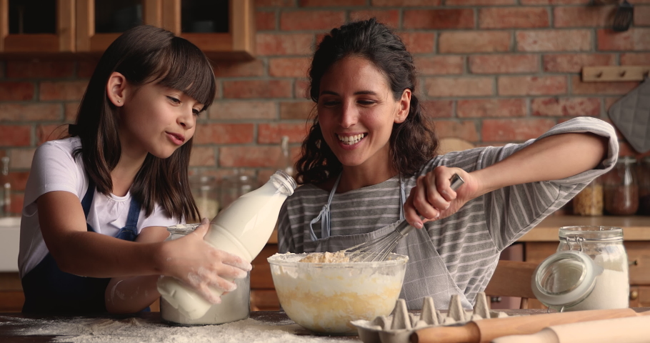 Young woman teach little 10s daughter cooking in cozy kitchen, preparing family recipe pie together, add milk and flour making dough for cake. Hobby, develop of child, share skills, motherhood concept Royalty-Free Stock Footage #1067355187