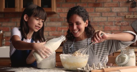Young woman teach little 10s daughter cooking in cozy kitchen, preparing family recipe pie together, add milk and flour making dough for cake. Hobby, develop of child, share skills, motherhood concept