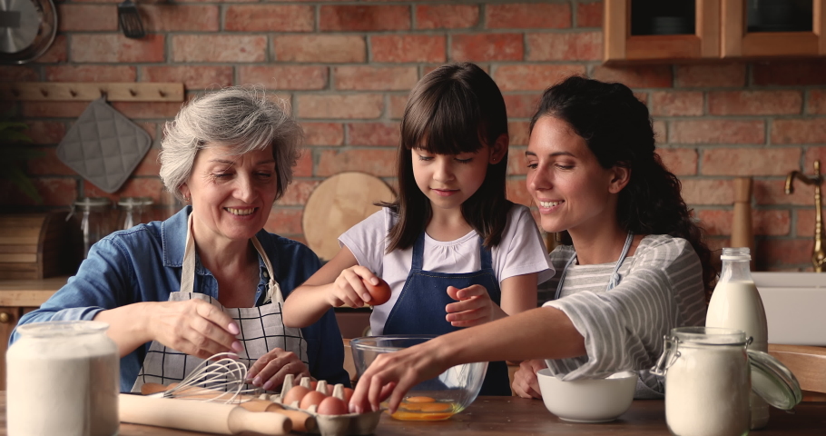 Three generation women, granny, grown up daughter little granddaughter cooking together in kitchen, add and beat eggs prepare family recipe cake. Time together, weekend leisure, hobby, cookery concept Royalty-Free Stock Footage #1067355205