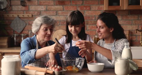 Three generation women, granny, grown up daughter little granddaughter cooking together in kitchen, add and beat eggs prepare family recipe cake. Time together, weekend leisure, hobby, cookery concept