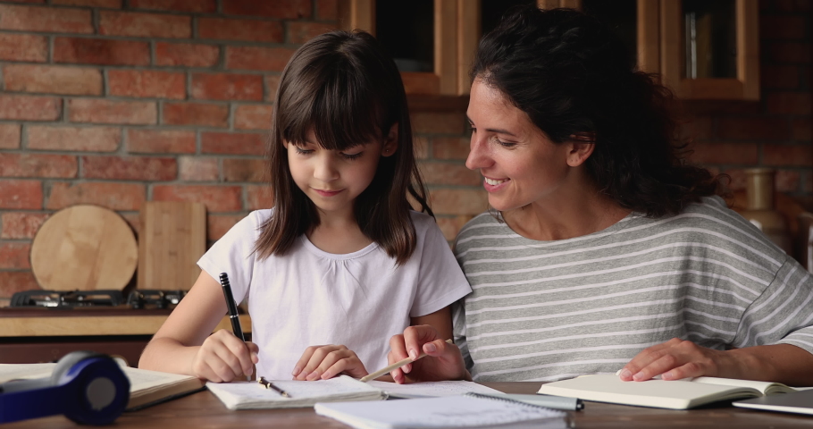 Caring mother helps to little daughter with homework. Tutor teach to schoolgirl explain hometask, new theme, make assignment together in domestic kitchen. Home-schooling, children education concept Royalty-Free Stock Footage #1067355241