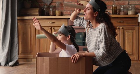 Small girl sit inside of carton box play pirates with mom in kitchen, wear drawn skull on caps, use paper tube like binocular watching into distance pretend be explorers. Playtime, fun at home concept
