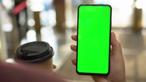 Back view of brunette holding chroma key green screen smartphone watching content.Shopping center. Department store. Mall. Shopping online. Gadgets and contemporary people concept.
