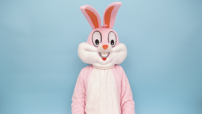 Easter bunny or rabbit or hare with basket of colored eggs, shows thumb finger up, having fun, dancing, celebrates Happy easter. Easter rabbit isolated on blue background | Shutterstock HD Video #1067363435