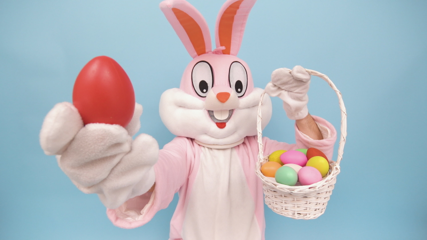 Easter bunny or rabbit or hare with basket of colored eggs, shows thumb finger up, having fun, dancing, celebrates Happy easter. Easter rabbit isolated on blue background Royalty-Free Stock Footage #1067363435