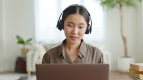 Portrait young Asian woman wearing headphone talking on video call conference or virtual meeting on laptop computer work from home