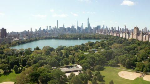 Manhattan Skyscrapers revealing behind beautiful Green Nature with Trees and Lake in Central Park, New York City, Aerial Wide View