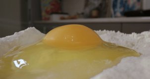 Making homemade dough. Egg with egg yolk and egg white hand breaks into white flour for baking cakes or bread on the kitchen table 4K time-lapse video.
