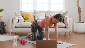 Sporty woman doing yoga and exercise at home, workout training online with coach on laptop in living room