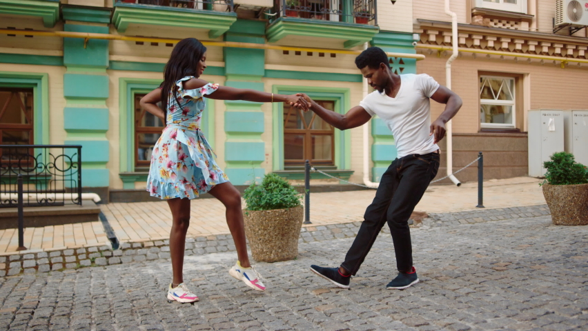 Full length sexy african dancers making footwork on street. Attractive afro man and woman making dance movements outdoors. African american couple dancing jive in city.