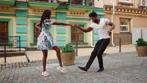 Full length sexy african dancers making footwork on street. Attractive afro man and woman making dance movements outdoors. African american couple dancing jive in city.