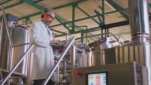 Quality expert in a white lab coat working in a milk factory. Milk factory interior with big vats. Milk factory equipment.