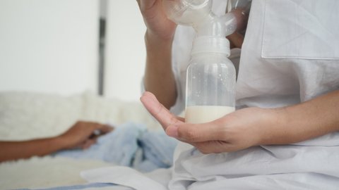 a woman uses a breast pump, young Asian mother pump feeding milk to a bottle for her baby, family at home, storage reserve,  improved lactation, breastfeed milk supply, feeding health care