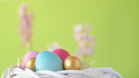 Colourful Easter eggs of pink, golden and green colour lie in straw spinning around on blurred light green background with pink and magenta hyacinth flowers. Spring Christian holidays design concept
