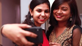 Two beautiful Indian woman talking with family online video call wearing ethnic traditional clothes for Diwali or another festival celebration