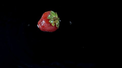 Strawberries roll in slow motion on a wet black surface. 