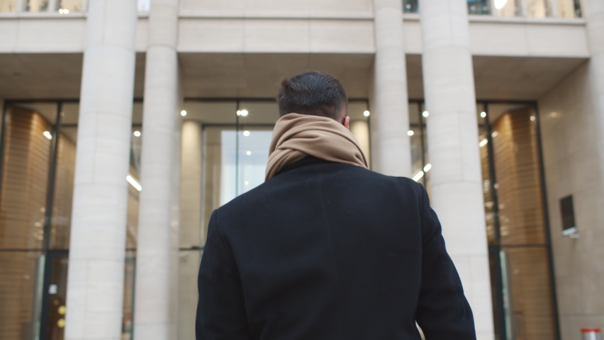 Back view of successful businessman entering business center. Confident male entrepreneur in coat and scarf walking through entrance doors in modern office building or apartment house Royalty-Free Stock Footage #1067390378