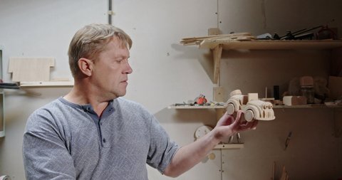 Skilled carpenter made a wooden car for his grandch and carefully examines the wooden toy in the home workshop and thinks to create a startup