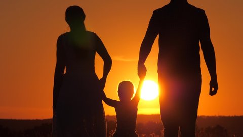 Happy family, little daughter is jumping, holding hands of dad and mom in park in sun. Child plays with dad and mom on field in light of sunset. Walk with a small child in nature. childhood, family