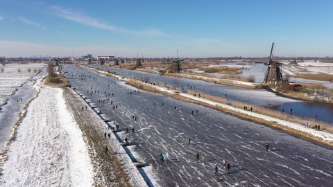 Aerial drone view of spectacular Winter landscape in Kinderdijk, the Netherlands. People ice skate on frozen canals past classic windmills (a welcome break from Covid-19 lockdown).