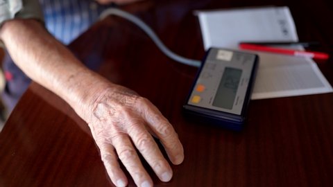 Old man with wrinkled hands using old-fashioned medical tonometer for measuring blood pressure and heartbeat pulse, electronic digital pressure gauge for checking hypertension and hypotension. Elderly