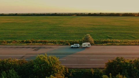 Aerial top view of offroad car and camper vehicle driving outdoors. Caravan van, trailer moving across country road, forest. Traveling, camping, adventure, vacation with motor home, exploring nature.