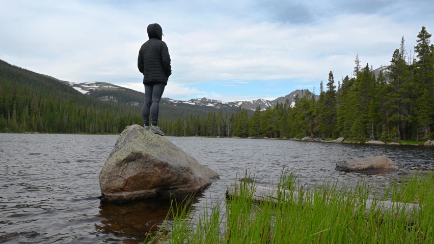 A hiker standing on a rock overlooks the scenic landscape from the shore of Finch Lake in Rocky Mountain National Park, Allenspark, Colorado, USA,