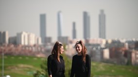 Two twin sisters walking through a green area with the city in the background - Powered by Shutterstock - Get 15% off with code: PIKWIZARD15