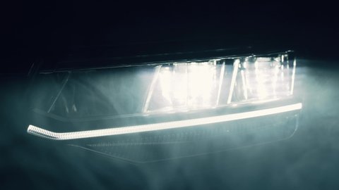 Switching of car LED headlights in night. New modern car headlamp in smoke, close up