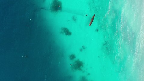 Aerial shot of the fisherman boat floating on turquoise Indian ocean waves near the Zanzibar white sand beach, Tanzania. Flying Drone point top view footage. Traveling and fishing industry concept 4K.