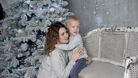 A beautiful little boy and his mother hug and pose for the camera during a New Year photo shoot in a photo studio. Close-up. Horizontal view. Family portrait. 4K