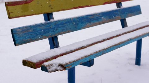 Winter background wooden bench for sitting is covered with snow, snowflakes fall on a wooden bench, winter cold. Colored bench in the snow