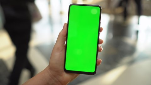 Back view of brunette holding chroma key green screen smartphone watching content.Shopping center. Department store. Mall. Shopping online. Gadgets and contemporary people concept.