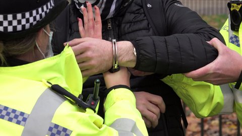 A police officer holds on to the handcuffs being used to restrain an arrestee.