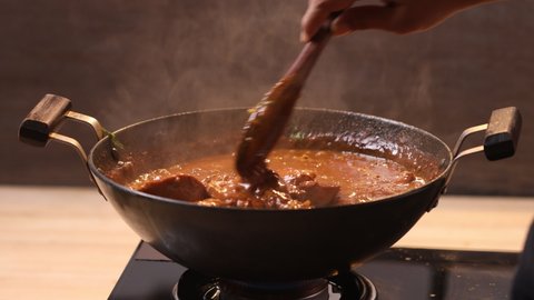 Boiling Chicken curry and adding garam masala and mixing to enhance its flavour ,in a cooking pan which is on gas stove with kitchen background,closeup videos.