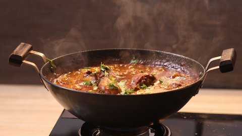 Boiling Chicken curry and adding garam masala to enhance its flavour ,in a cooking pan which is on gas stove with kitchen background,closeup videos.