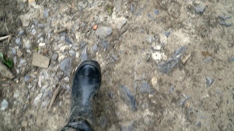 Slow motion footage looking down at ground while someone is purposefully walking in black wellington boots through countryside terrain. Top down view with space for copy text.