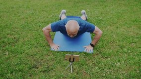 Powerful Old Male Athlete Makes Push Up while Looking on Smartphone Screen. Watching Live or Video Tutorial with Help of his Instructor Online on Cellphone. Workout and Self Motivation. Slow Motion.