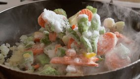 Frozen vegetables are cooked in a frying pan, highlighting steam.