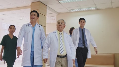 Group of Asian team of doctors, nurses and assistants walking through the hallway of the hospital. Professional medical experience doctors walking indoor and working for save the lives. Slow Motion. 