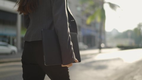 close-up Video Slow-motion. A white business Asian woman in a black suit walking on the street side. Carrying a laptop to work at the office in the morning.
