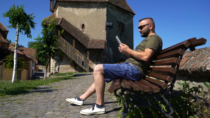Young man browsing Internet on tablet sitting on bench in city